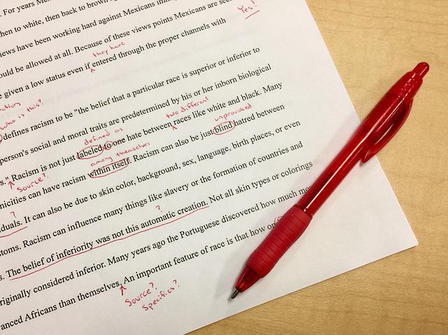 A printed piece of paper, most likley being an essay, is on the table along with a red pen. There are red correction marks on the paper.