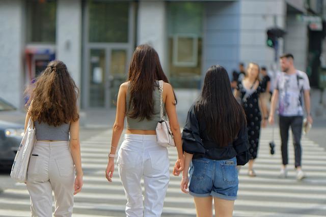 A group of 3 girls walk across the street in a city. The camera points towards their backs.