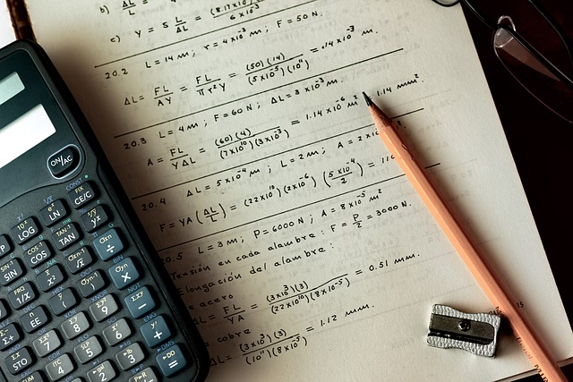 A picture of a math notebook open to show math notes. A calculater, pencil, pencil sharpener, and glasses are also on the table.