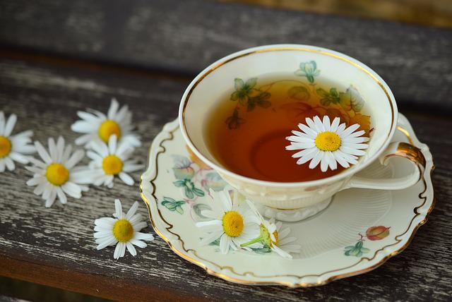 A teacup sits on a wooden table, which is decorated with daisy flowers.